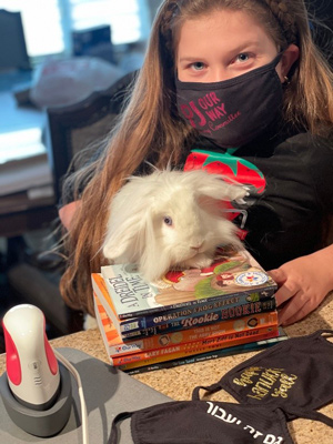 A masked girl sitting with a rabbit on a stack of books